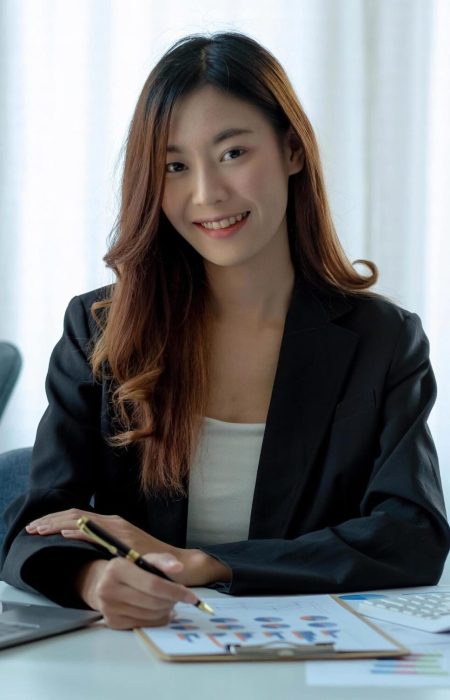 charming-asian-woman-working-at-the-office-using-a-laptop-looking-at-the-camera-free-photo