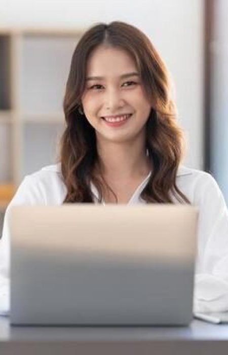 charming-asian-woman-working-at-the-office-using-a-laptop-looking-at-the-camera-photo